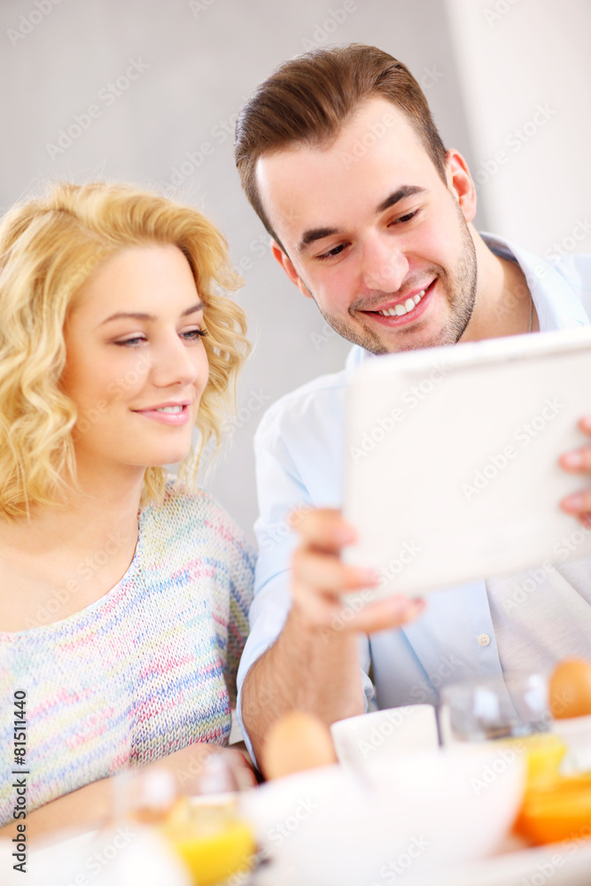 Happy couple eating breakfast and using tablet Happy couple eating breakfast and using tablet