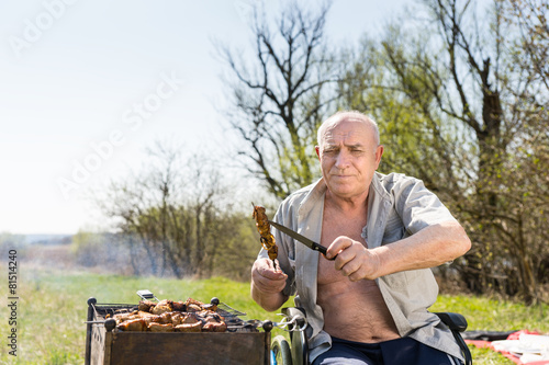 Sitting Elderly Man Holding Grilled Meat and Knife