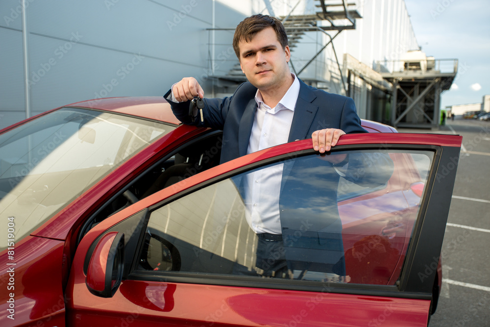 handsome man in suit leaning against new car and showing keys handsome man in suit leaning against new car and showing keys