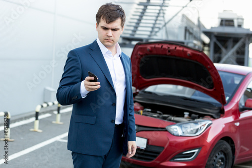 businessman standing at broken car and using telephone