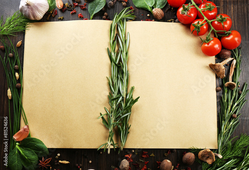 Open recipe book with fresh herbs, tomatoes and spices