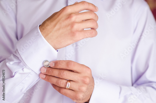 The man puts on a white shirt cufflinks