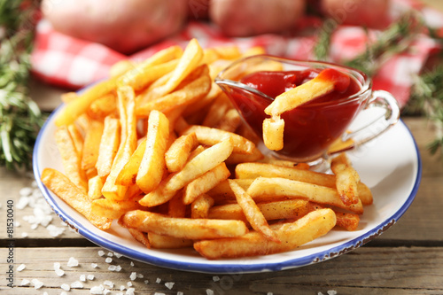 Tasty french fries on plate, on wooden table background