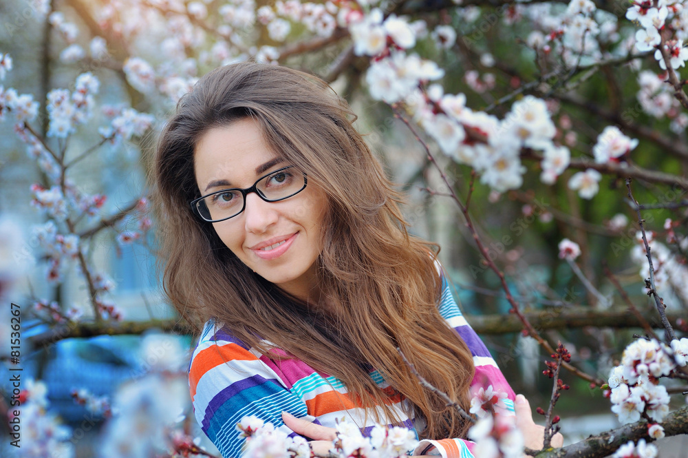 Brunette in glasses on a background of a blossoming tree in spri Brunette in glasses on a background of a blossoming tree in spri