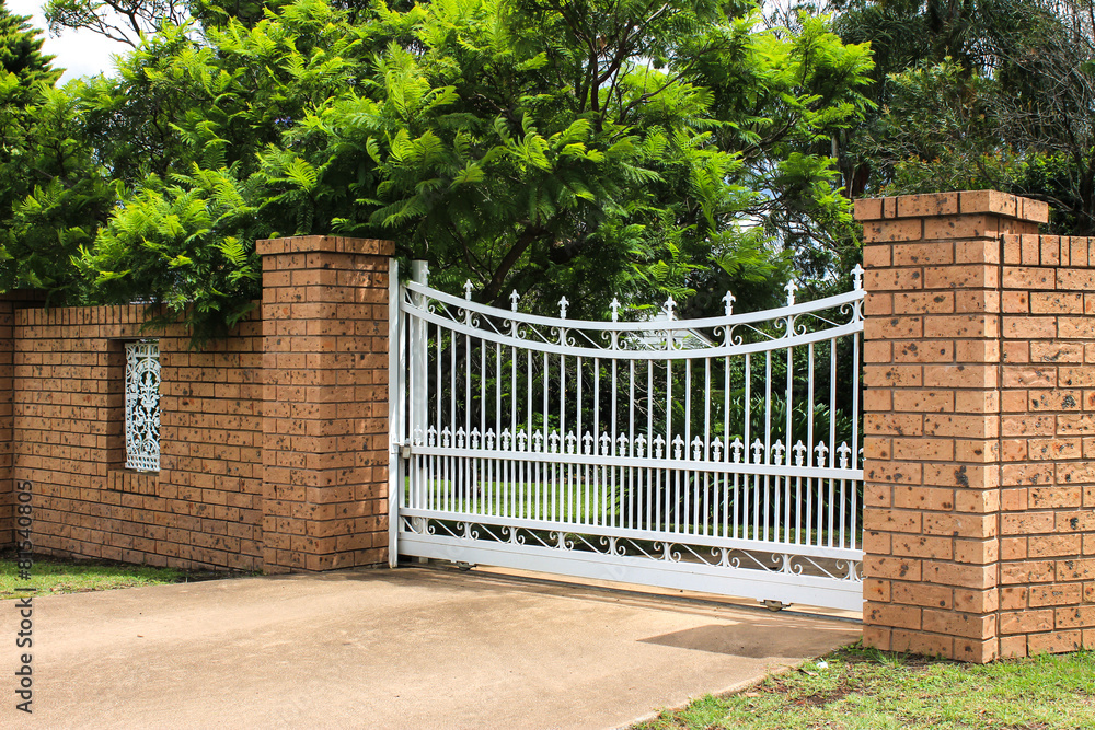 White wrought iron driveway entrance gates in brick fence - obrazy, fototapety, plakaty 