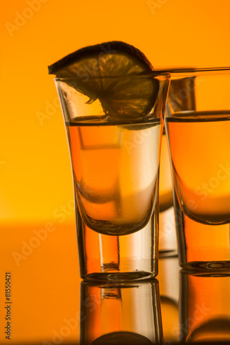 Tequila shot with a slice of lime on the glass orange background
