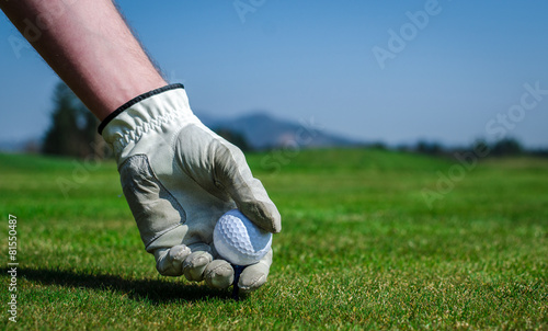 Hand with a glove is placing a tee with golf ball in the ground.