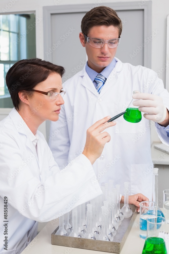 Scientists examining attentively beaker with green fluid Scientists examining attentively beaker with green fluid