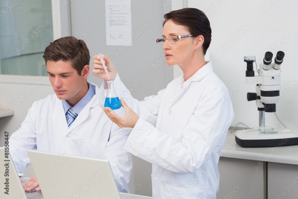 Scientists working with laptop and using a beaker Scientists working with laptop and using a beaker