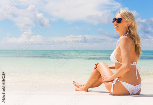 Beautiful woman in white bikini sitting on the beach