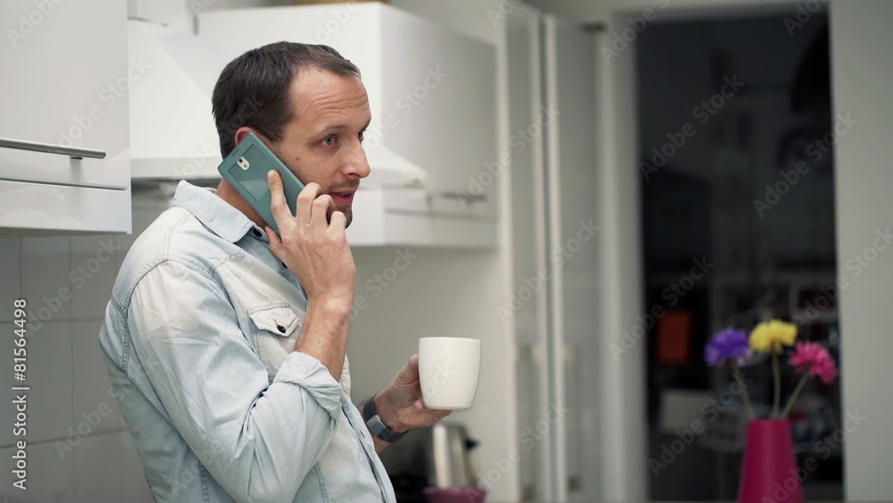 Happy, young man talking on cellphone and drinking coffee in kit Happy, young man talking on cellphone and drinking coffee in kit