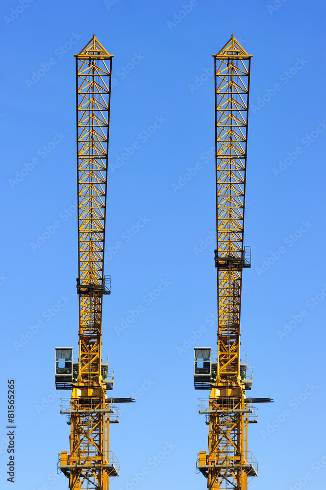 Two construction yellow cranes towers isolated on blue sky Two construction yellow cranes towers isolated on blue sky