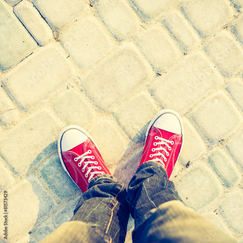 Young man feet in red sneakers on cobbled road