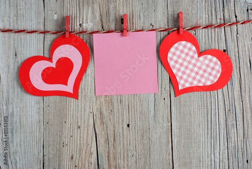 Paper hearts and blank note on old wooden background