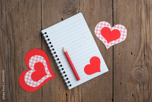 Notebook with hearts and pencil on old wooden background