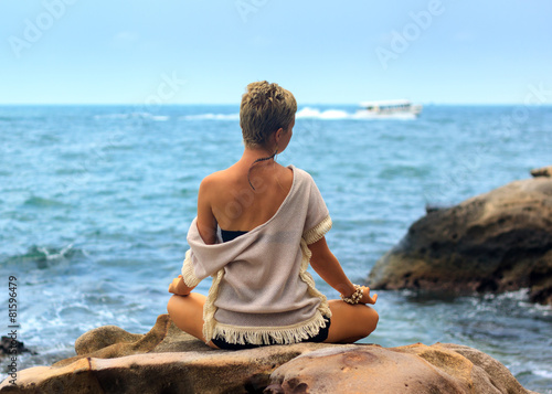 Beautiful woman seated in yoga pose at blue sea background