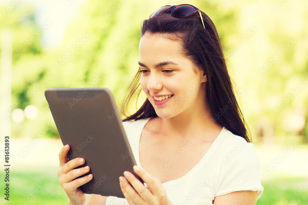 Obraz premium smiling young girl with tablet pc sitting on grass