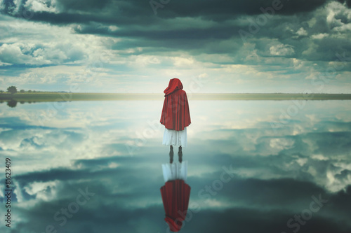 Red hooded woman in a strange landscape with clouds