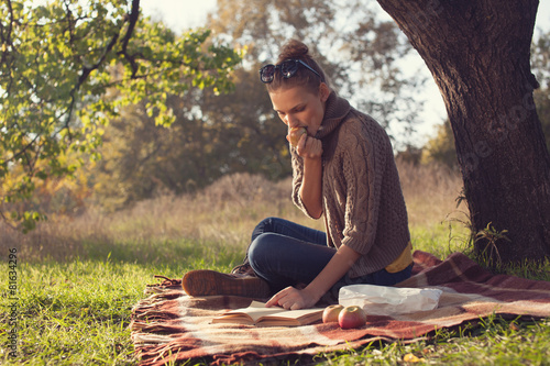 Cuadro en lienzo Young woman reading a books and eating apple outdoors
