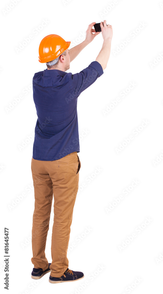 Backview of an engineer in construction helmet stands and using