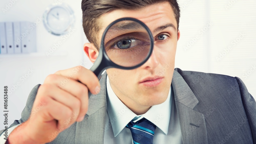 Composite image of businessman looking through magnifying glass Composite image of businessman looking through magnifying glass