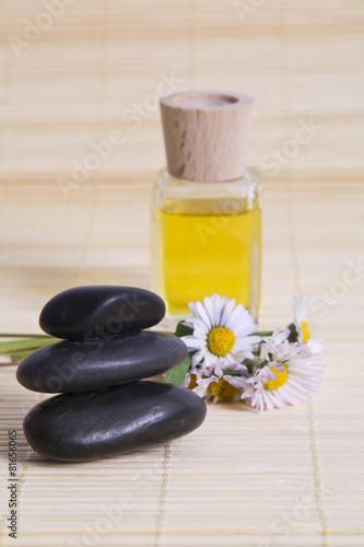 oil, daisies and stones on wooden background