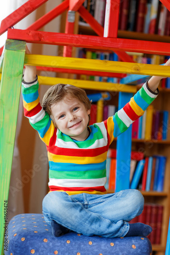 Little blond kid boy playing in selfmade wooden colorful house