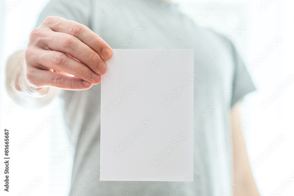 Man in a grey t-shirt holding a blank white piece of paper Man in a grey t-shirt holding a blank white piece of paper