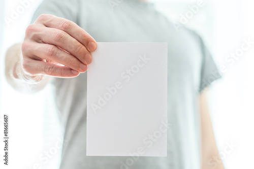 Man in a grey t-shirt holding a blank white piece of paper © Gajus