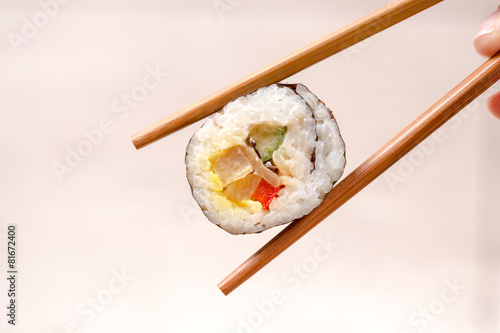 Hand holding sushi roll using chopsticks