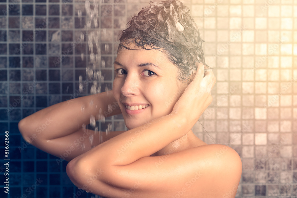Naklejka premium Frau massiert Shampoo in ihre Haare unter der Dusche