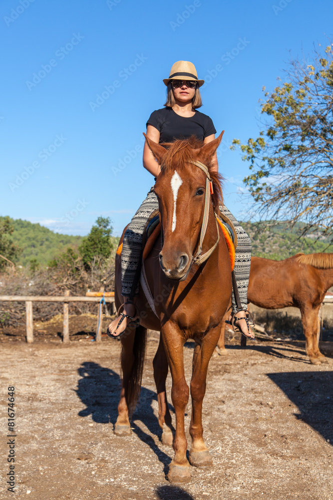 Girl in hat riding on a brown horse