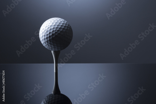 Golf ball on tee isolated on dark blue reflective background.