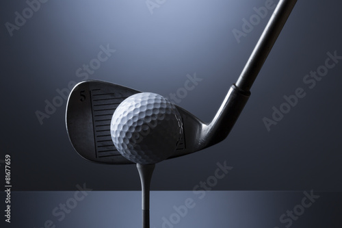 Golf ball on tee with club isolated on dark blue background.