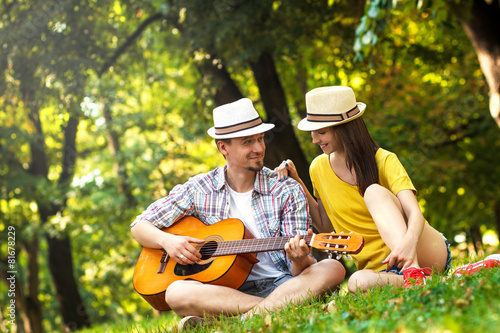 Young couple in love playing acoustic guitar in the park