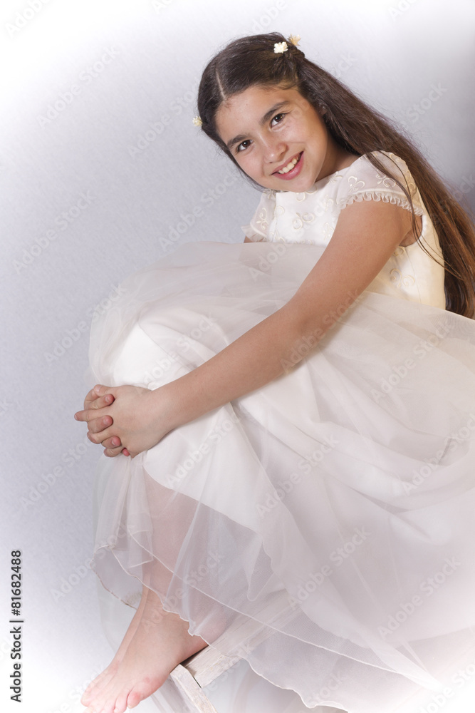 Smiling girl with communion dress possing sitting on a chair and Smiling girl with communion dress possing sitting on a chair and