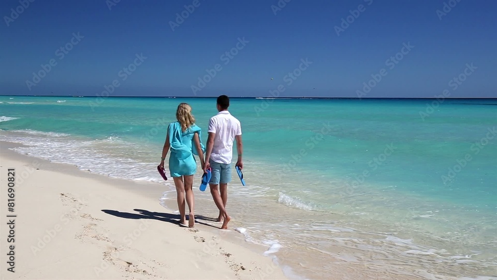 Young couple with slippers walking along the beach Young couple with slippers walking along the beach