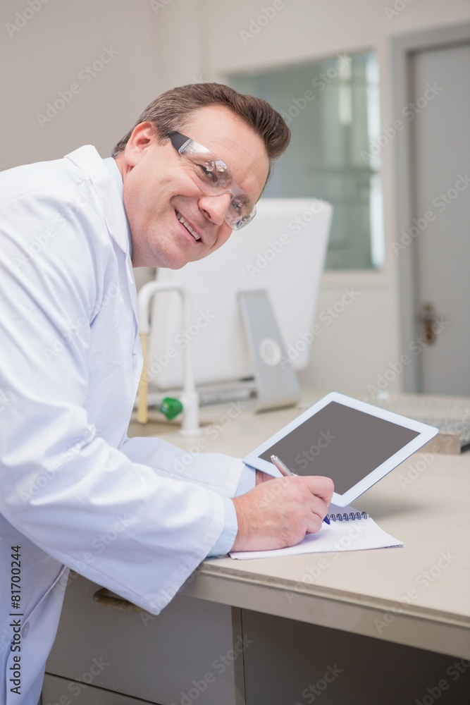 Smiling scientist holding tablet writing on notebook Smiling scientist holding tablet writing on notebook