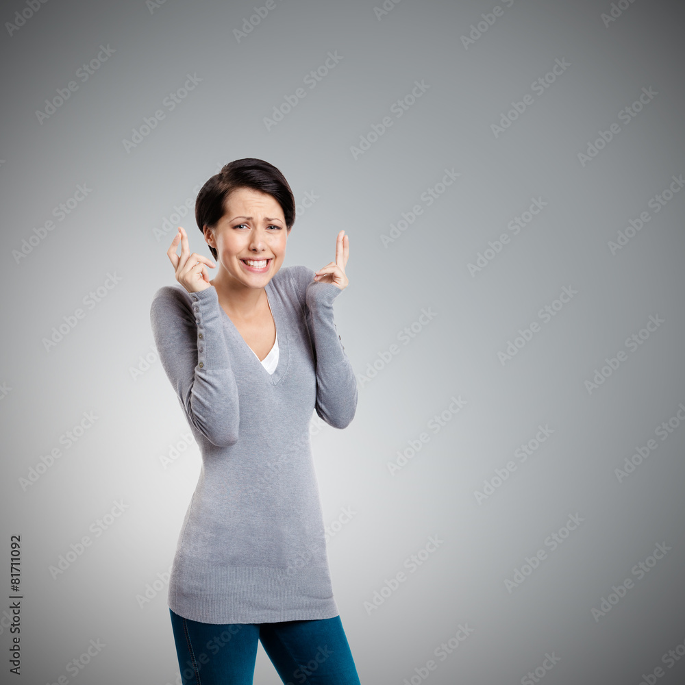 Hoping young woman shows crossed fingers, isolated on grey