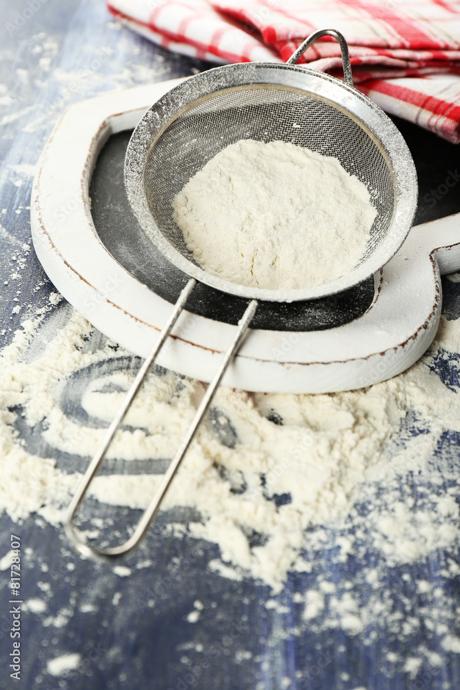 Fototapeta premium Sifting flour through sieve on wooden table, closeup