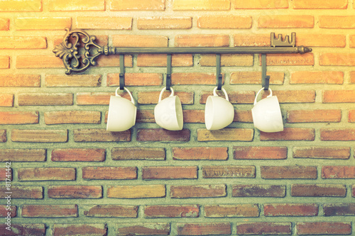 Coffee cups hanging on hooks in front of brick wall ( Filtered i