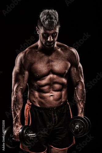 muscular young man lifting weights on dark background