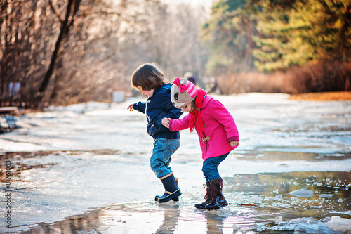 toddler boy and girl walking in early spring puddle
