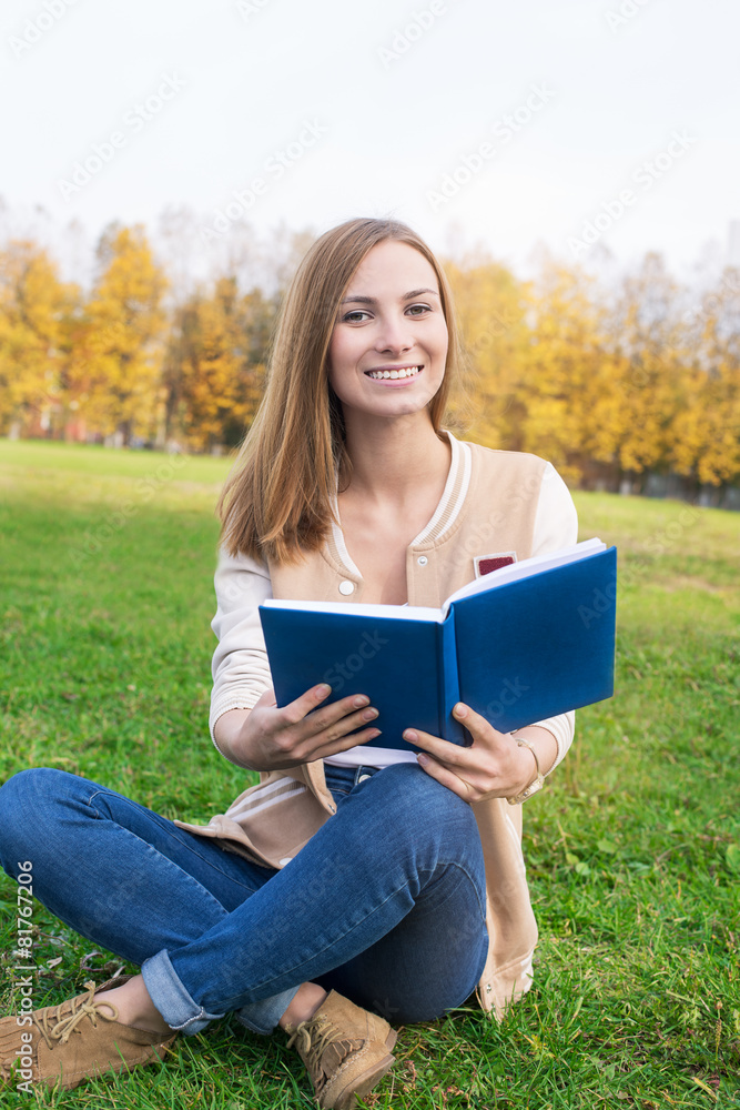 Student sitting on green grass with opened blue book Student sitting on green grass with opened blue book