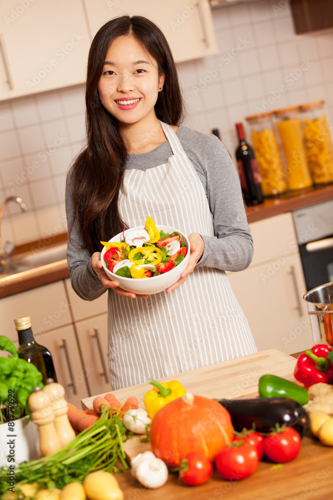 Asian smiling woman with a colorful salad in her hands is standi