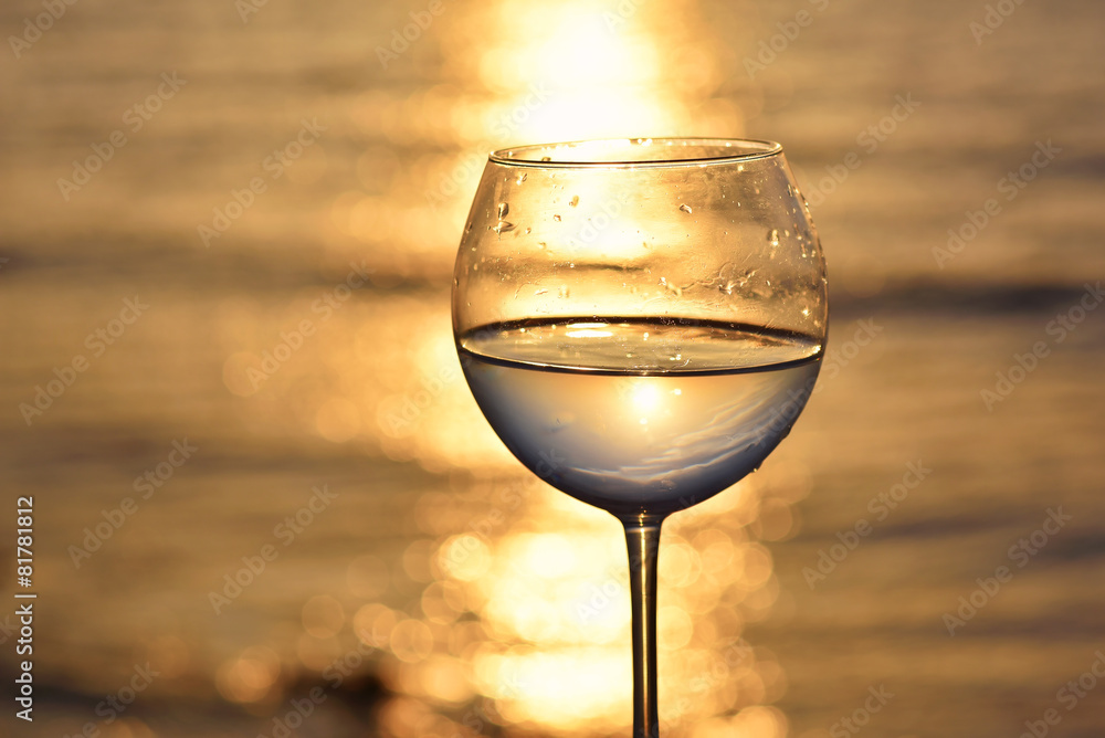 glass with white wine above sunset sea ocean