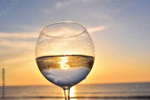 glass with white wine above sunset sea ocean