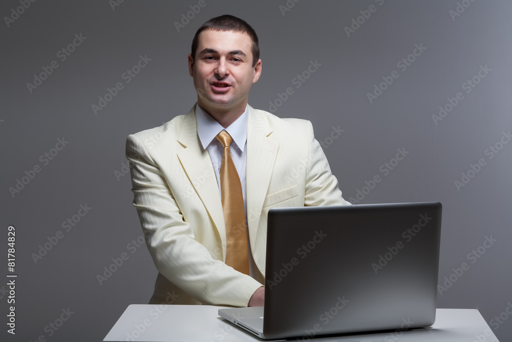 A man in a white suit sitting with a laptop. Makes hand gestures