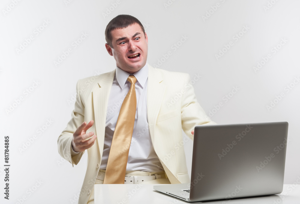 A man in a white suit sitting with a laptop. Makes hand gestures