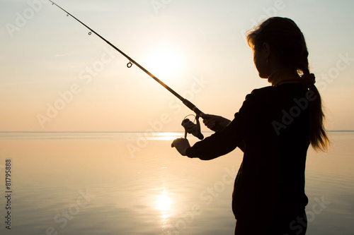silhouette of a young girl fishing at sunset near the sea
